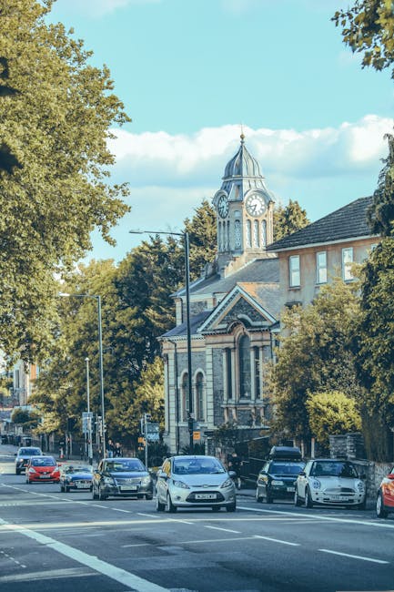 A narrow residential street during daytime in West Hampstead, featuring a cobblestone pathway bordered by a brick wall on the left and modern white and grey brick buildings with bay windows on the right. The street curves gently and is mostly empty, with a few leafless trees visible in the background. There are black bollards and lamp posts along the pavement, indicating a pedestrian-friendly area. This setting illustrates the typical environment where professional house removals, such as those offered by Man and Van West Hampstead, might take place, including residential streets suitable for home relocation or furniture transport during packing and moving processes.